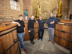 Dr Markus Rondé and Dr Adam Robinson with Annandale Distillery's Mark Trainor and David Ashton. The men are standing in Annandale Distillery and are leaning against wooden vats